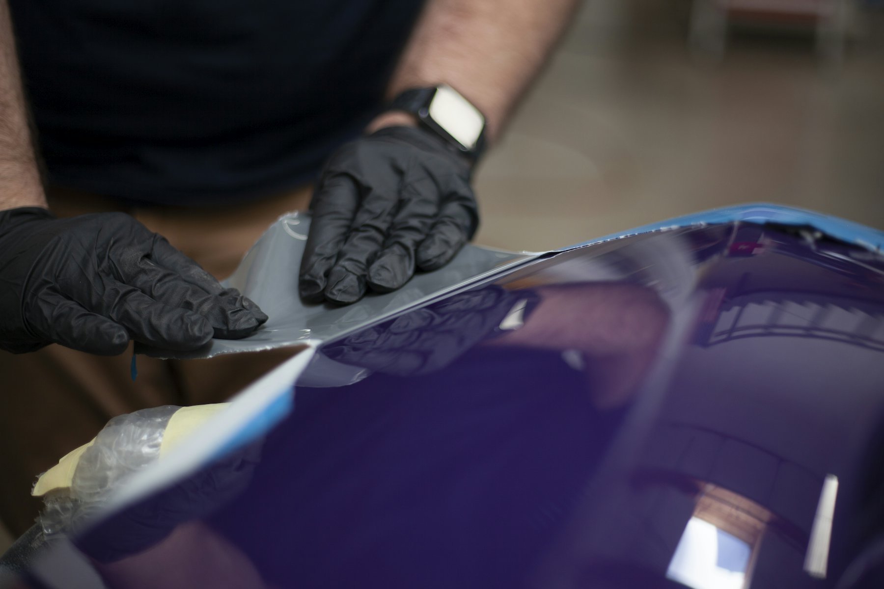 Hände in Schutzhandschuhen an einer tief violett lackierten Fahrzeugfläche